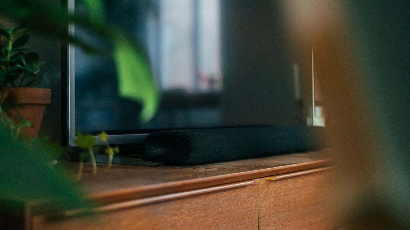 En svart soundbar ligger på en träfärgad TV-bänk.