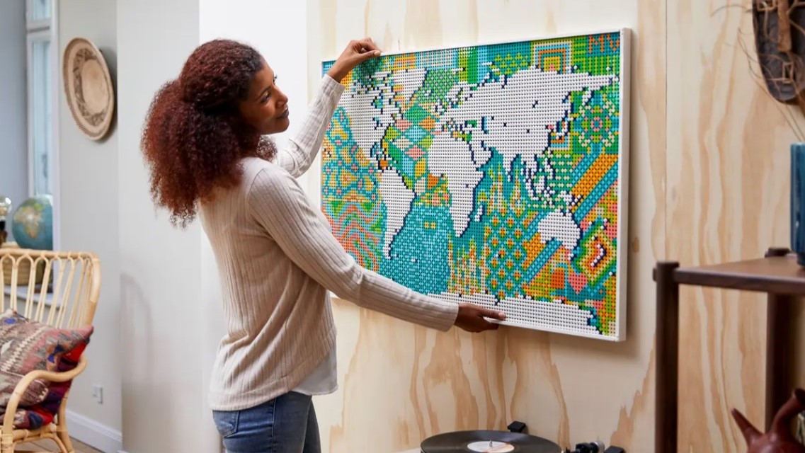 En kvinna hänger upp en färdig Lego-version av världskartan på väggen.