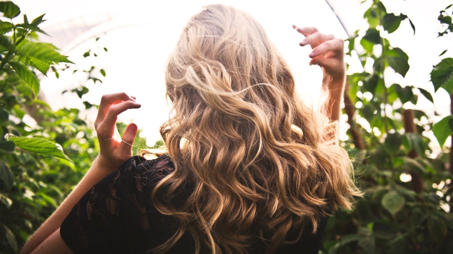 En kvinna sedd bakifrån med lockigt, blont hår som täcker ryggen.
